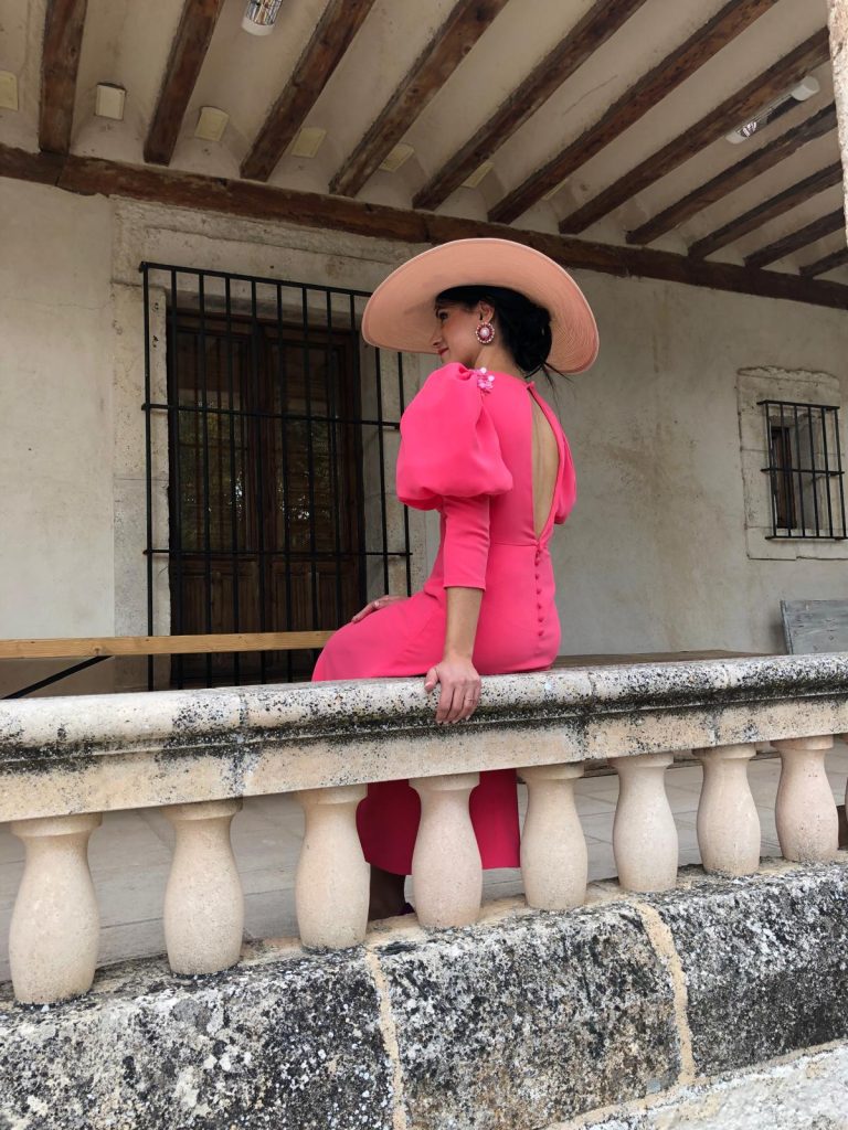 Mujer posando con el vestido y sombrero sentada en la barandilla de piedra
